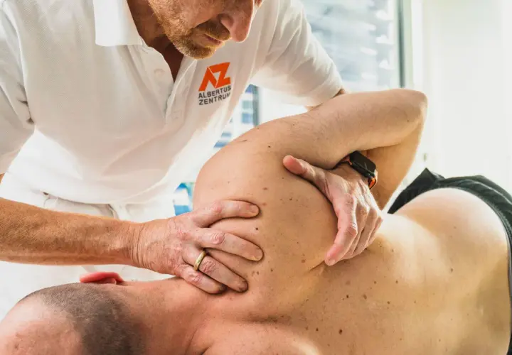 Osteopath behandelt Schulterschmerzen. Hände des Therapeuten am Schulterblatt eines Patienten.