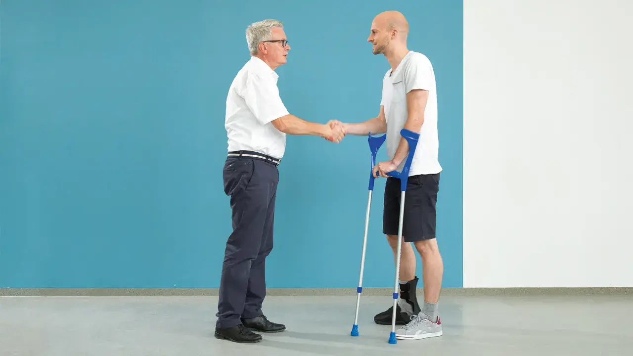 Arzt schüttelt Hand eines Patienten mit Krücken und Orthese am Fuß nach einer Calcaneusfraktur.