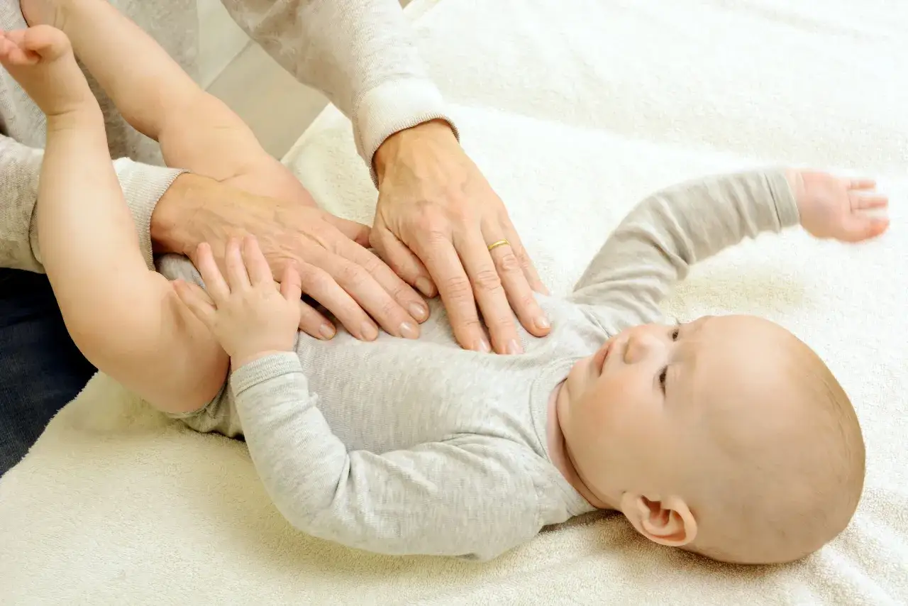 Sanfte Hände einer Osteopathin behandeln den Bauch eines Babys. Sanfte Berührungen zur Unterstützung der Entwicklung von Neugeborenen.