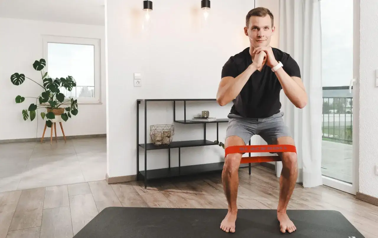 Mann macht Kniebeugen mit Widerstandsband, trainiert die Flexion im Knie.