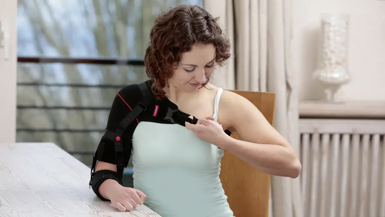 Frau legt eine Armorthese an, um ihre Schulter zu stabilisieren.