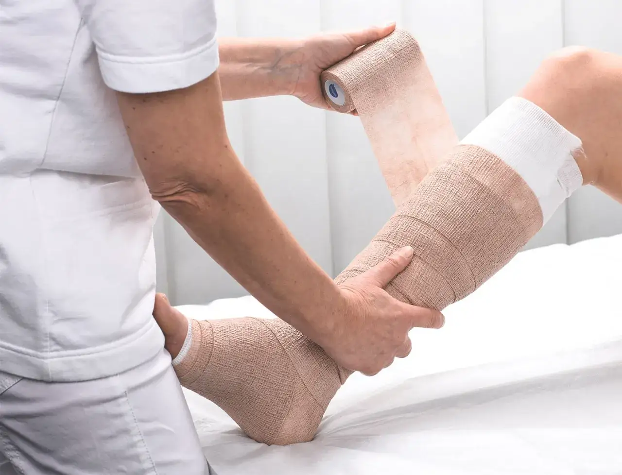 Eine Person wickelt einen Verband um ein Bein für Kompression.