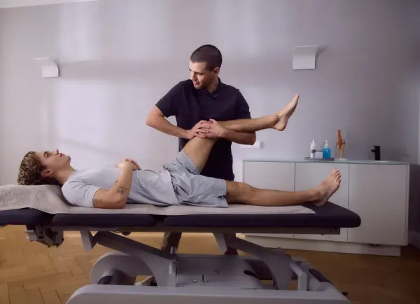 Physiotherapeut dehnt das Bein eines Patienten auf einer Liege. Die Knie-Schiene nach OP wird sanft bewegt, um die Beweglichkeit wiederherzustellen.